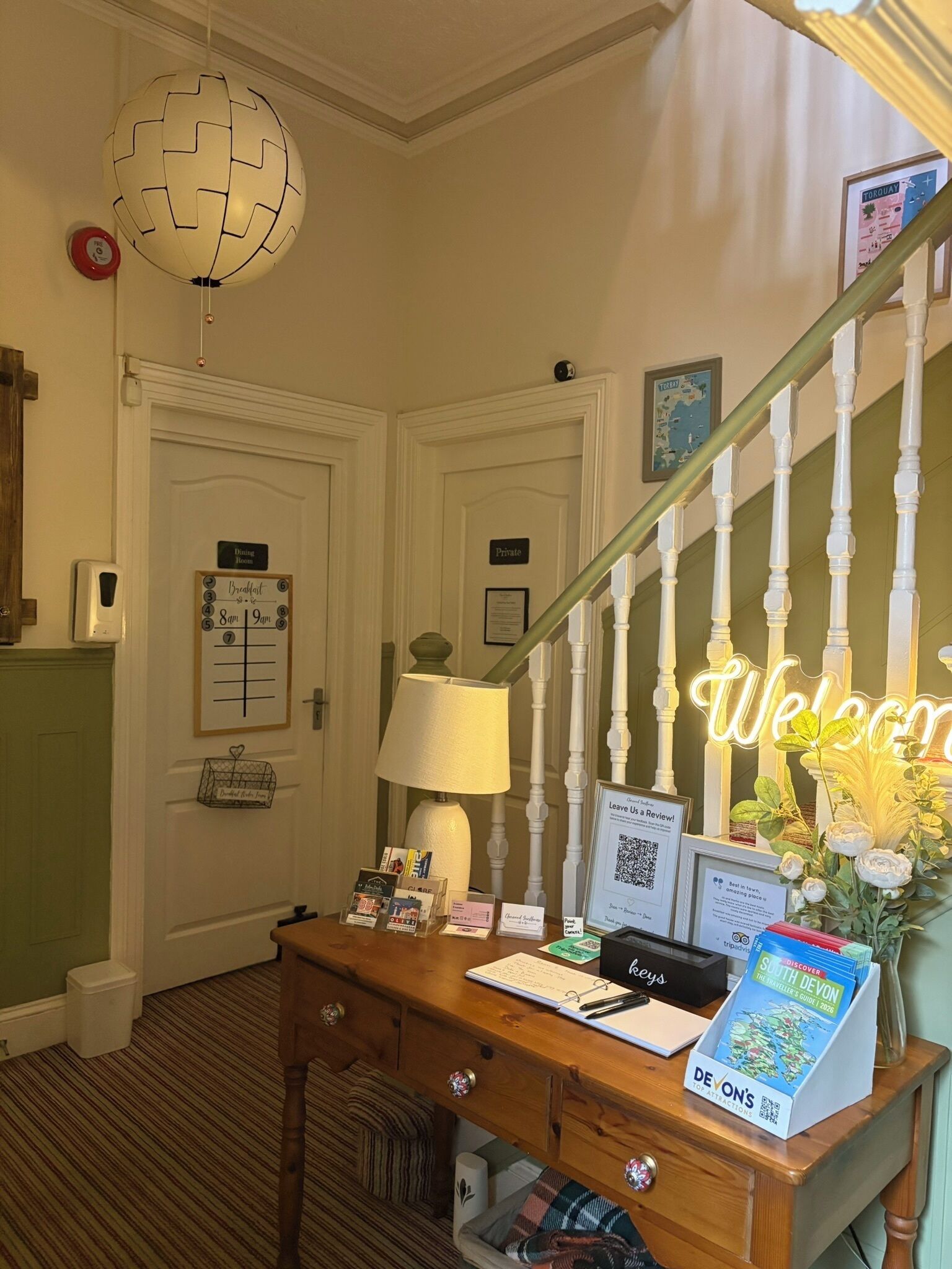 A reception desk with a lamp, a 'Welcome' sign, a framed map, and a 'Dining Room' sign.