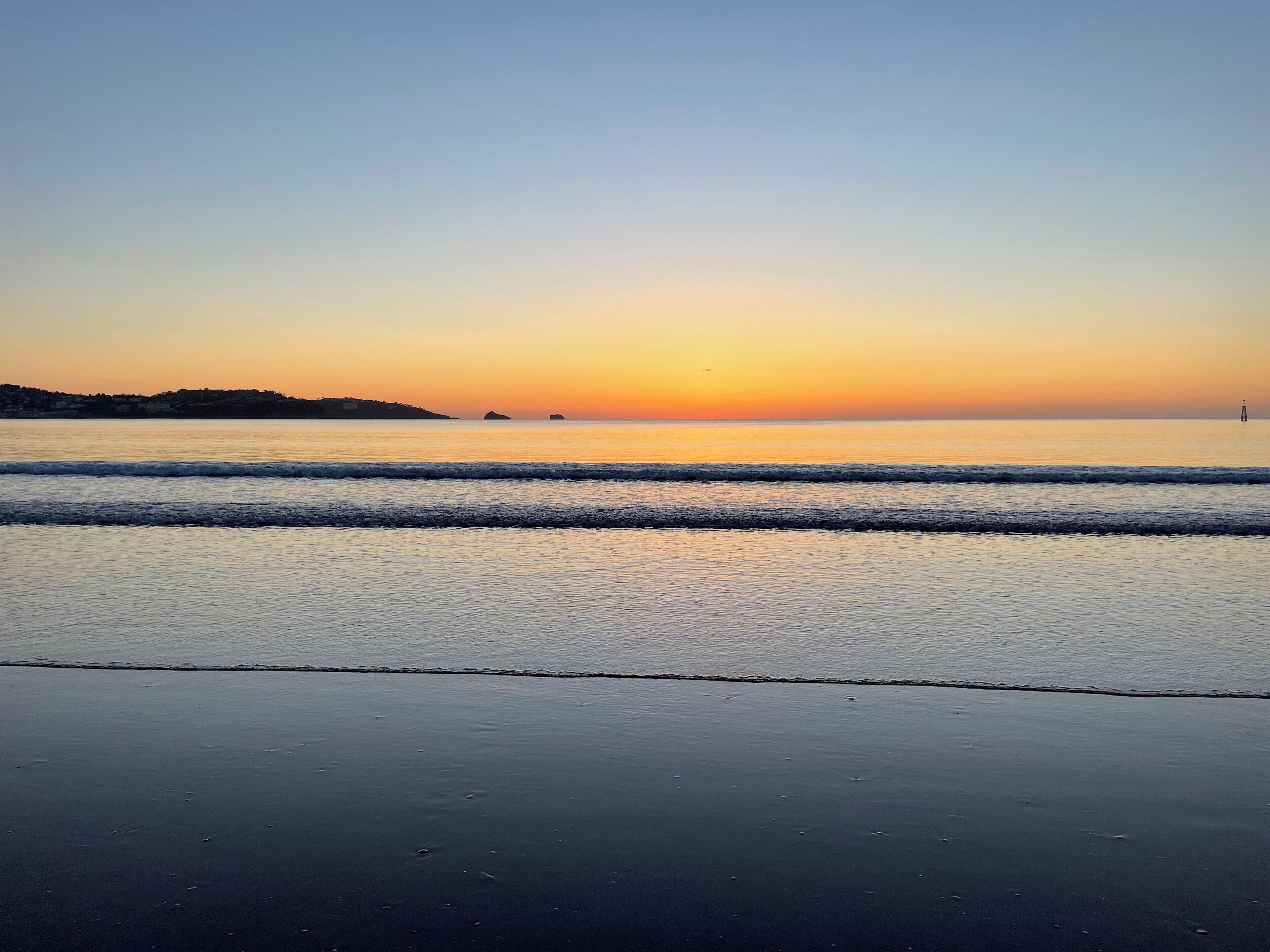 A beach with calm waves and a sunset.