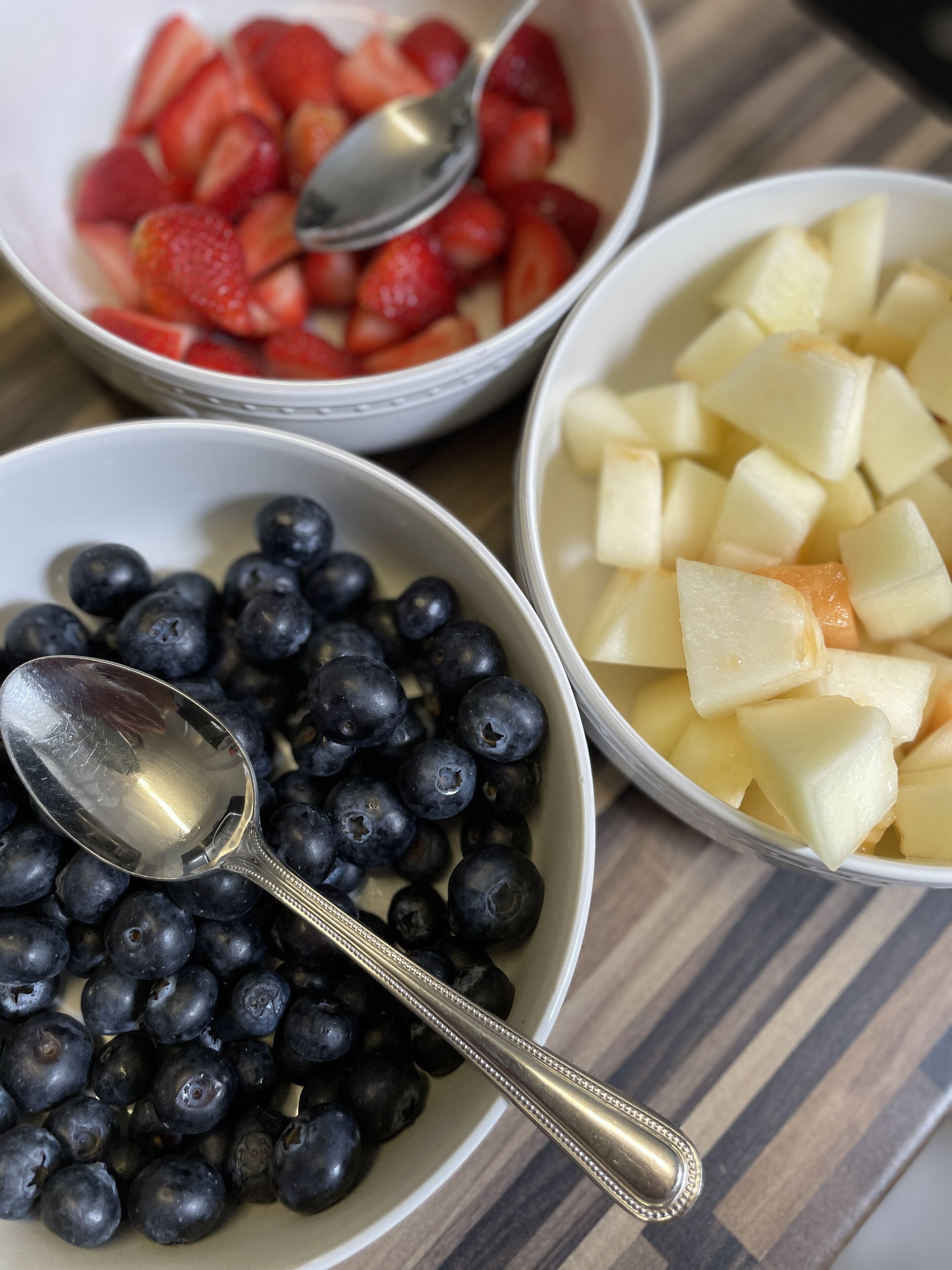 Drie schalen fruit met lepels op een tafel.