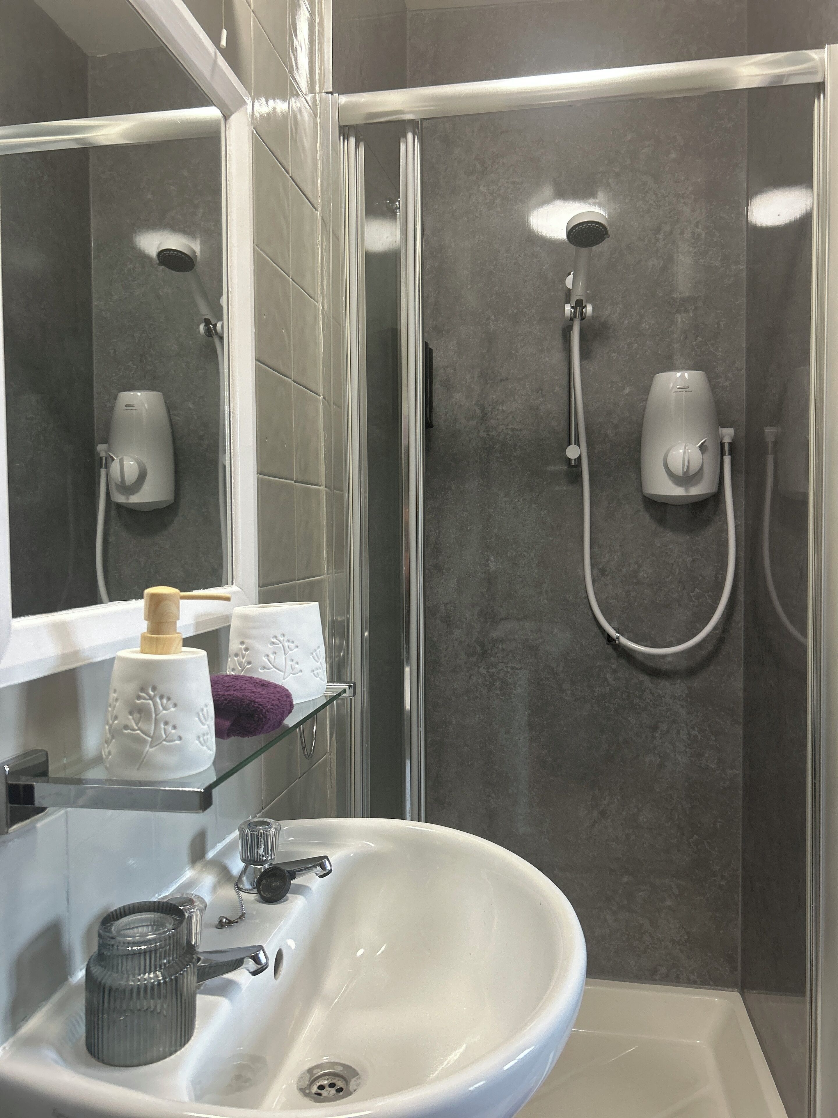 A modern bathroom with a glass shower enclosure, a white sink, and a mirror.