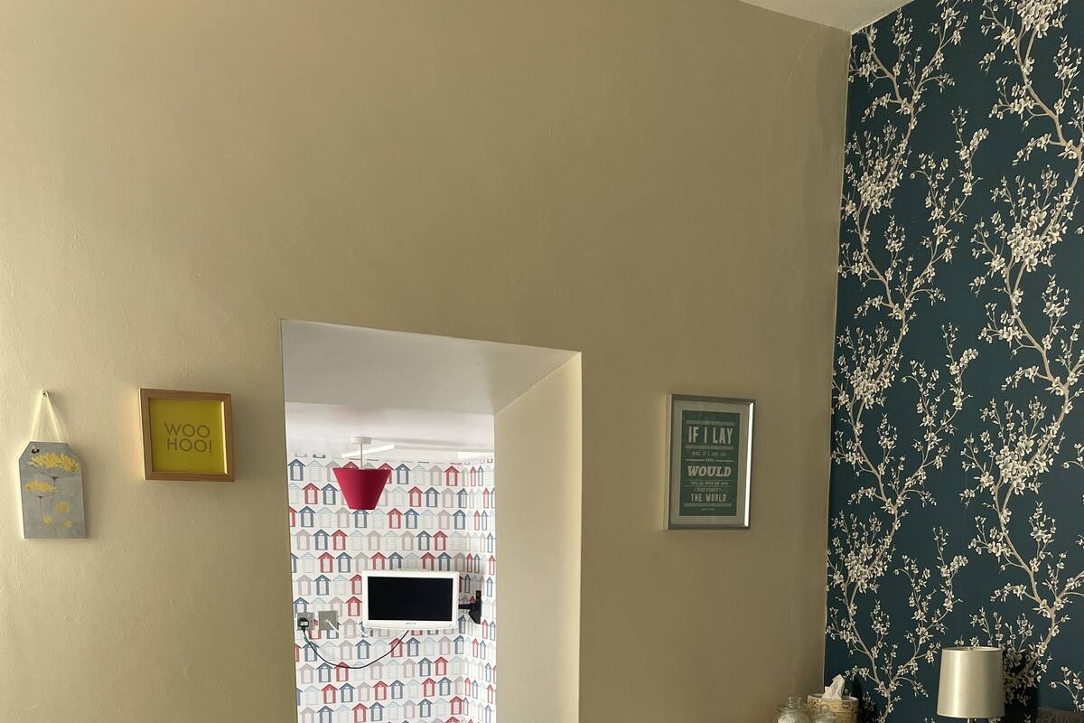 Une chambre d’hôtel avec un lit, une table de chevet, une lampe et une vue sur une autre chambre dont le papier peint est à motifs.