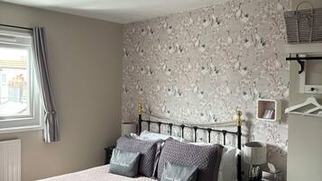 A neatly made bed with pillows, a bedside table with a lamp, a chair, and a wall with a floral pattern.