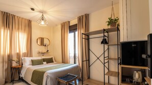 A neatly arranged hotel room with a bed, a small table with a lamp, a shelf with a TV and a coffee maker, and a hanging plant.