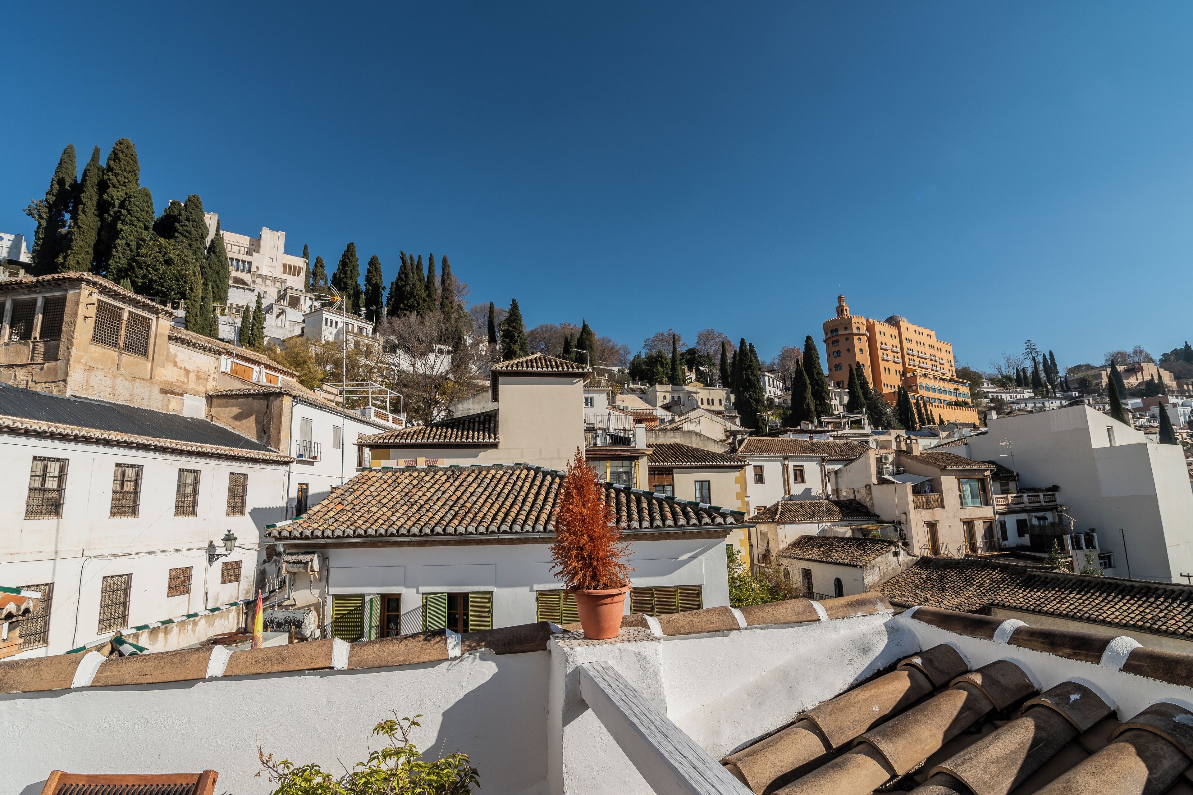 Un pueblo tradicional europeo con tejados de tejas color terracota, edificios blancos y un edificio naranja destacado al fondo.