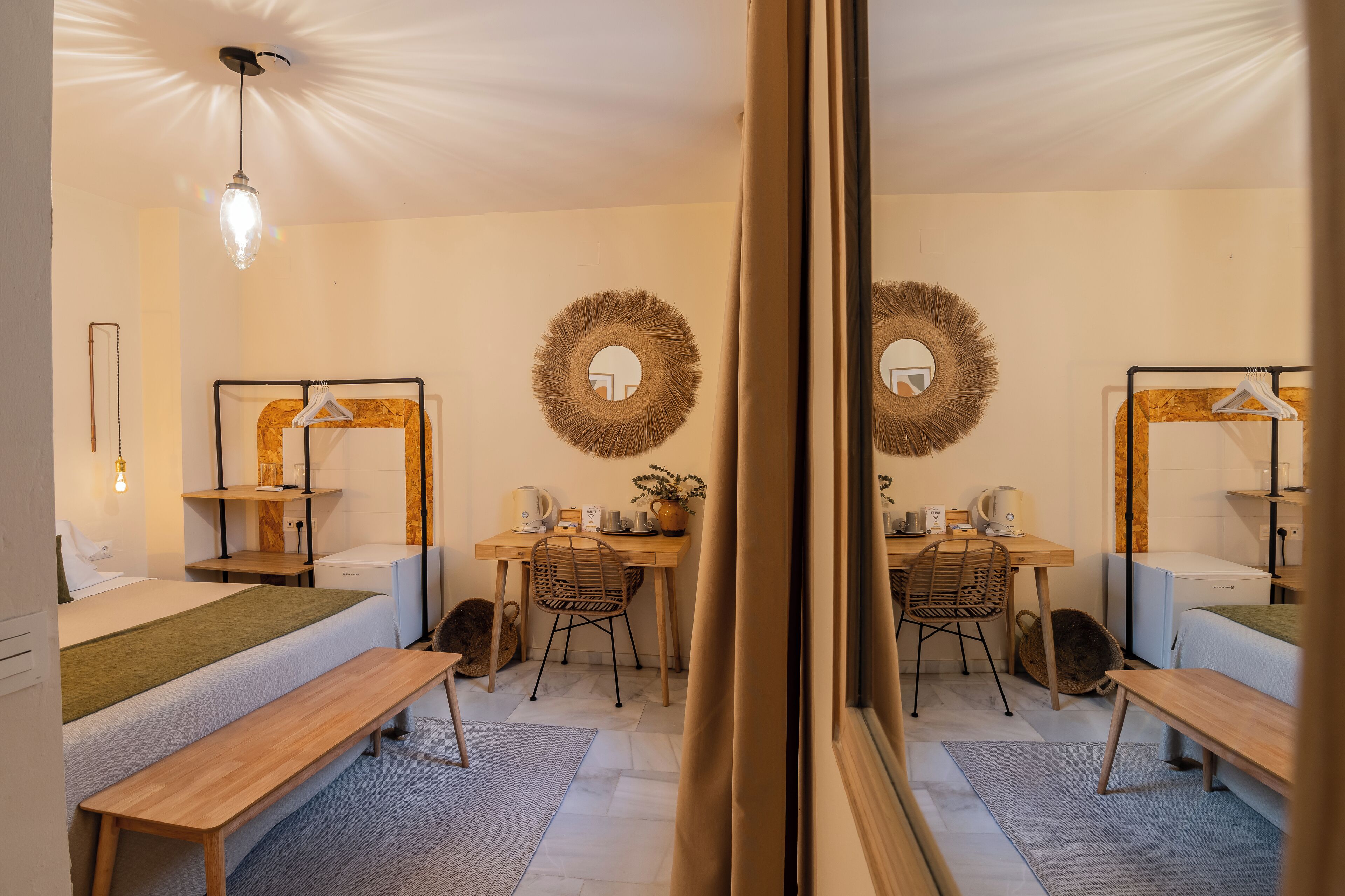 A well-lit, modern hotel room with a bed, a desk, a chair, a bench, and a mirror.