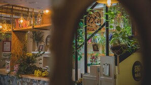 A cozy interior with shelves holding plants and decorative items, a wooden counter, and a visible sign with text.