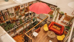 A multi-level living space with a staircase, a red sofa, yellow chairs, and various plants.