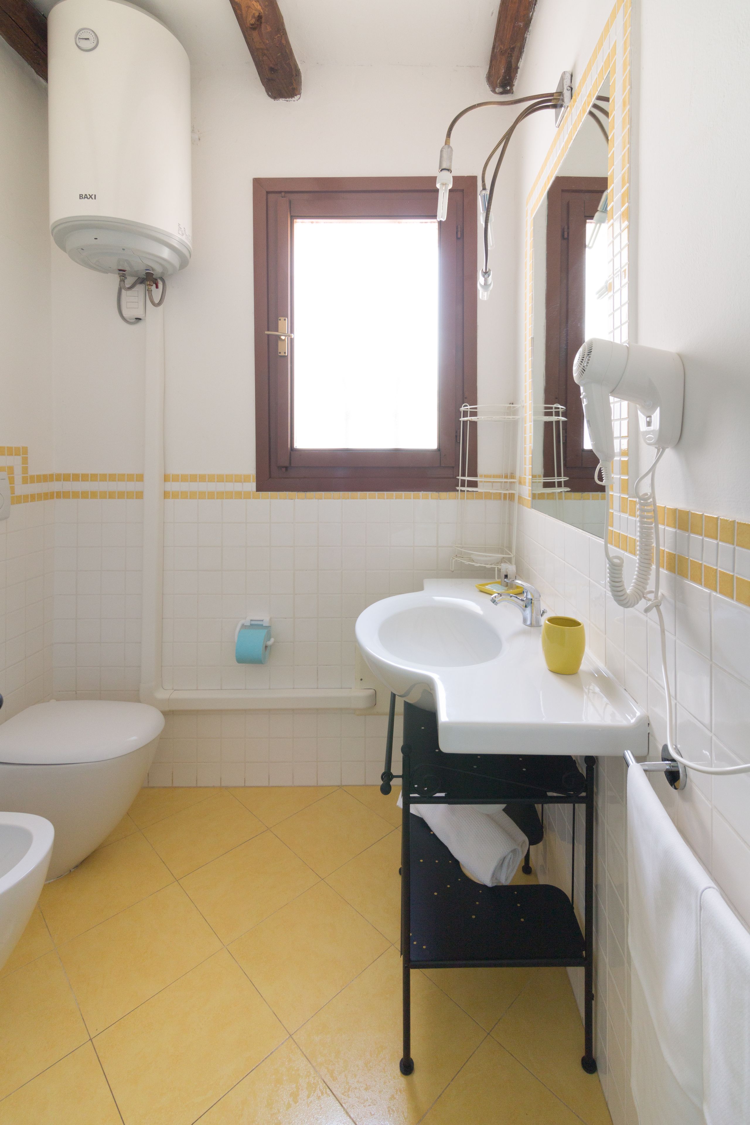 Un baño con inodoro, lavamanos y una ventana sobre el lavamanos.