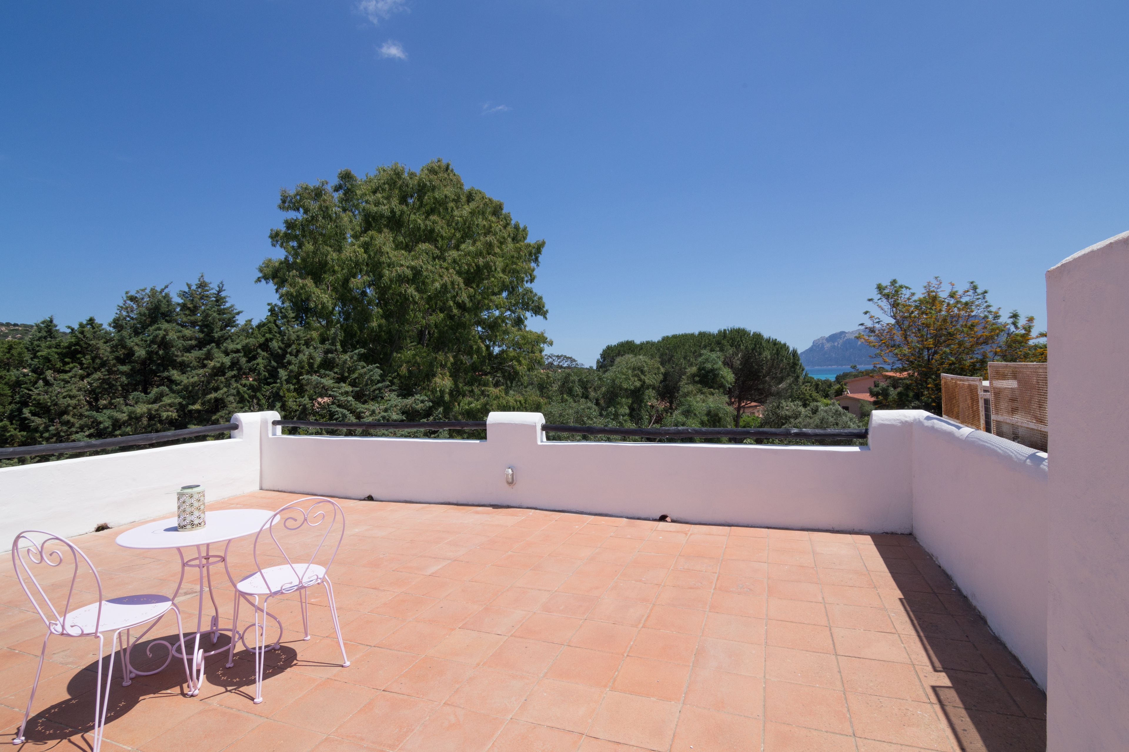 Une terrasse avec une table et des chaises, un mur blanc et une vue sur les arbres et les montagnes.