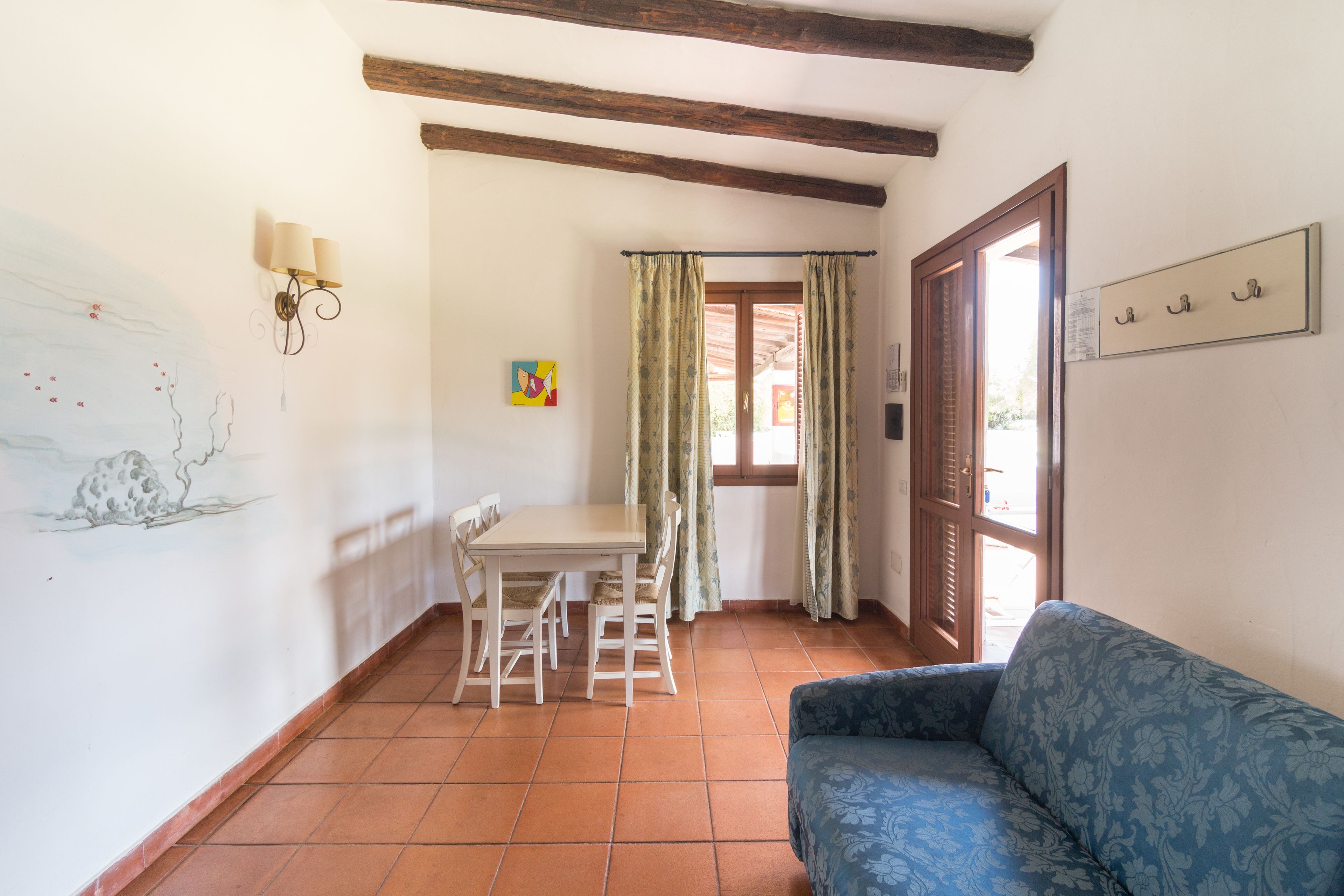 A room with a dining table and chairs, a sofa, a wall with a painting, and a door with a window.