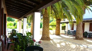 An outdoor patio area with palm trees, covered seating, and a brick floor. - White Sand Residence (Olbia)