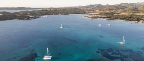 An aerial view of a coastal area with clear turquoise waters, several boats, and rocky outcrops.
