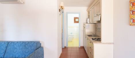 A narrow hallway with a blue sofa on the left, a kitchen area on the right, and a door leading to a bathroom.