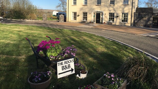 A building with a sign reading "THE ROCKS B&B" and a garden with potted plants. - The Rocks Bed & Breakfast (Crumlin)
