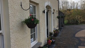 A building with a textured facade, a paved driveway, and flower boxes along the side. - The Rocks Bed & Breakfast (Crumlin)