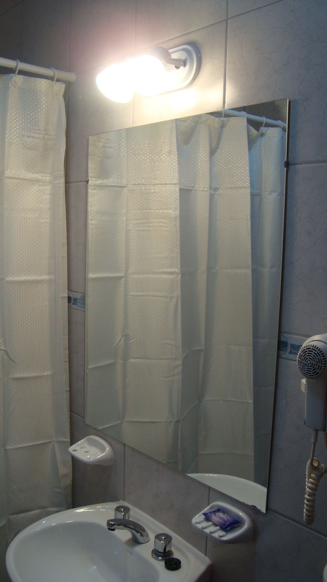 A bathroom with a shower curtain, a sink, a mirror, and a hairdryer.