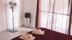 Een hotelkamer met een bed, een ventilator, een verwarming en een raam met gordijnen.