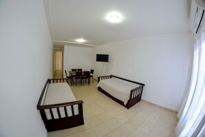 Une chambre avec deux lits simples, une table à manger avec des chaises, un téléviseur fixé au mur et un ventilateur de plafond.