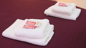 Twee netjes opgevouwen witte handdoeken met roze zakjes op een structuurrijk rode ondergrond.