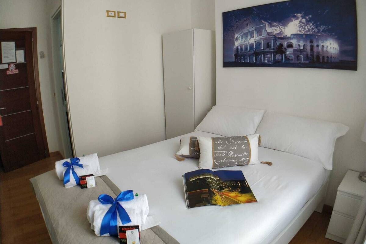 A neatly made bed with white linens, a pillow with a quote, a book, and a wrapped gift.