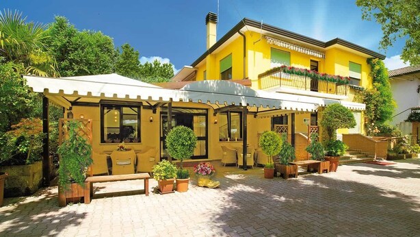 Un bâtiment jaune doté d’un espace extérieur couvert avec des sièges, de plantes en pot et d’une terrasse en briques.
