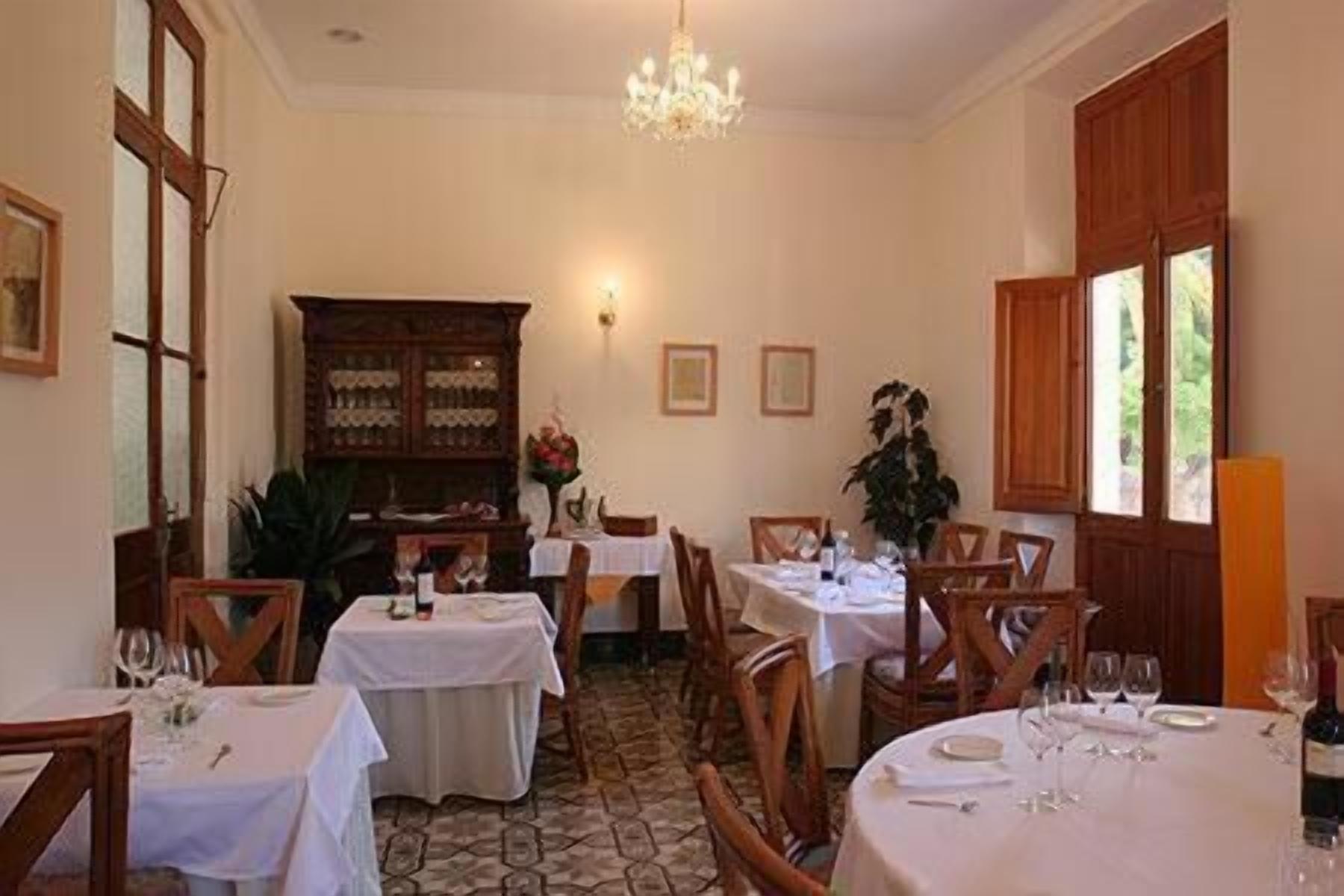 A dining area with tables set for a meal, a chandelier, and a wooden cabinet with glass doors.