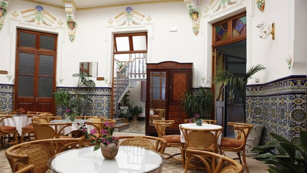 Un interior tradicional con mesas redondas, sillas de mimbre, una escalera y azulejos decorativos.