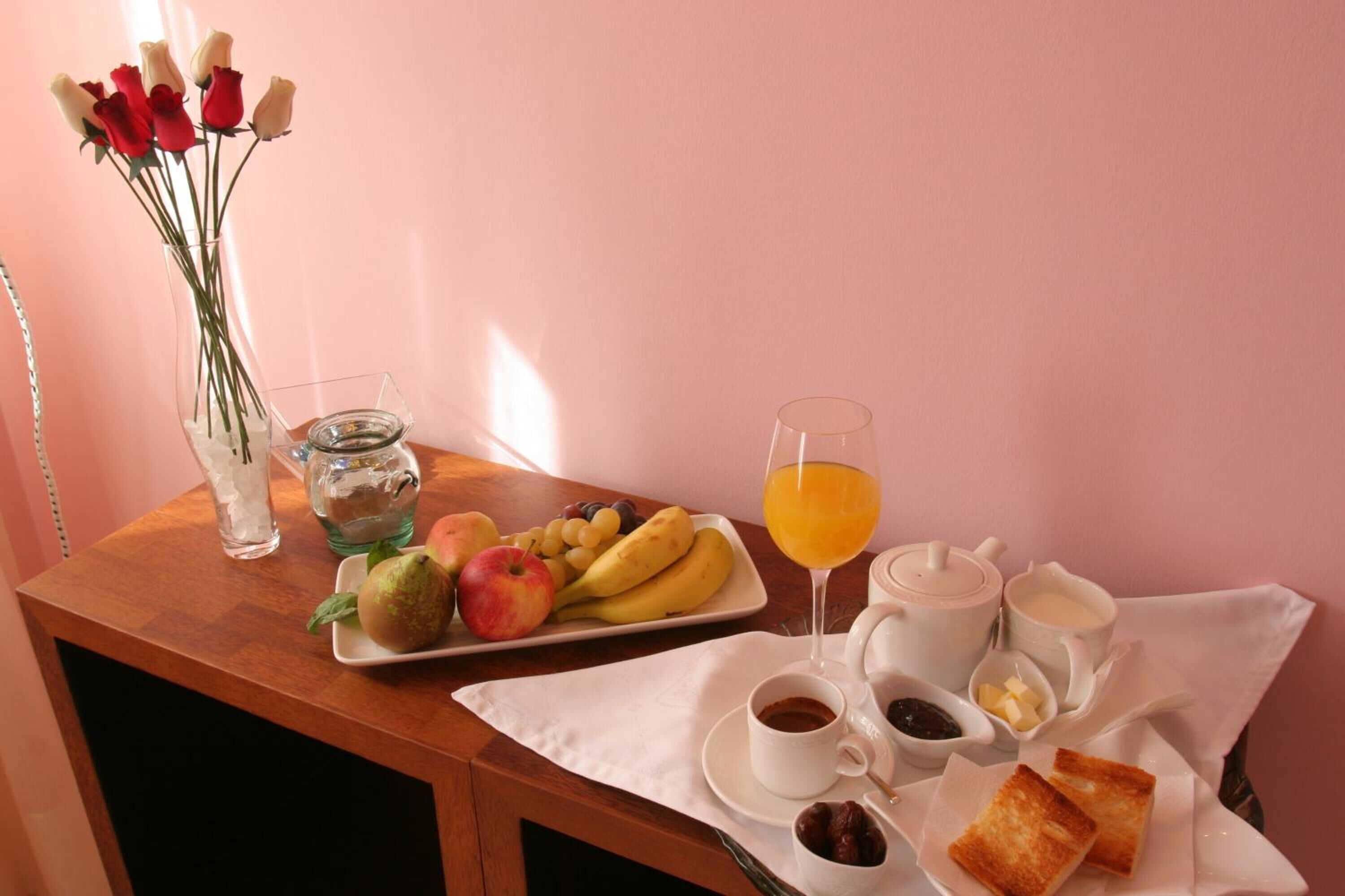 Una mesa de desayuno con frutas, un vaso de zumo de naranja, café y tostadas.