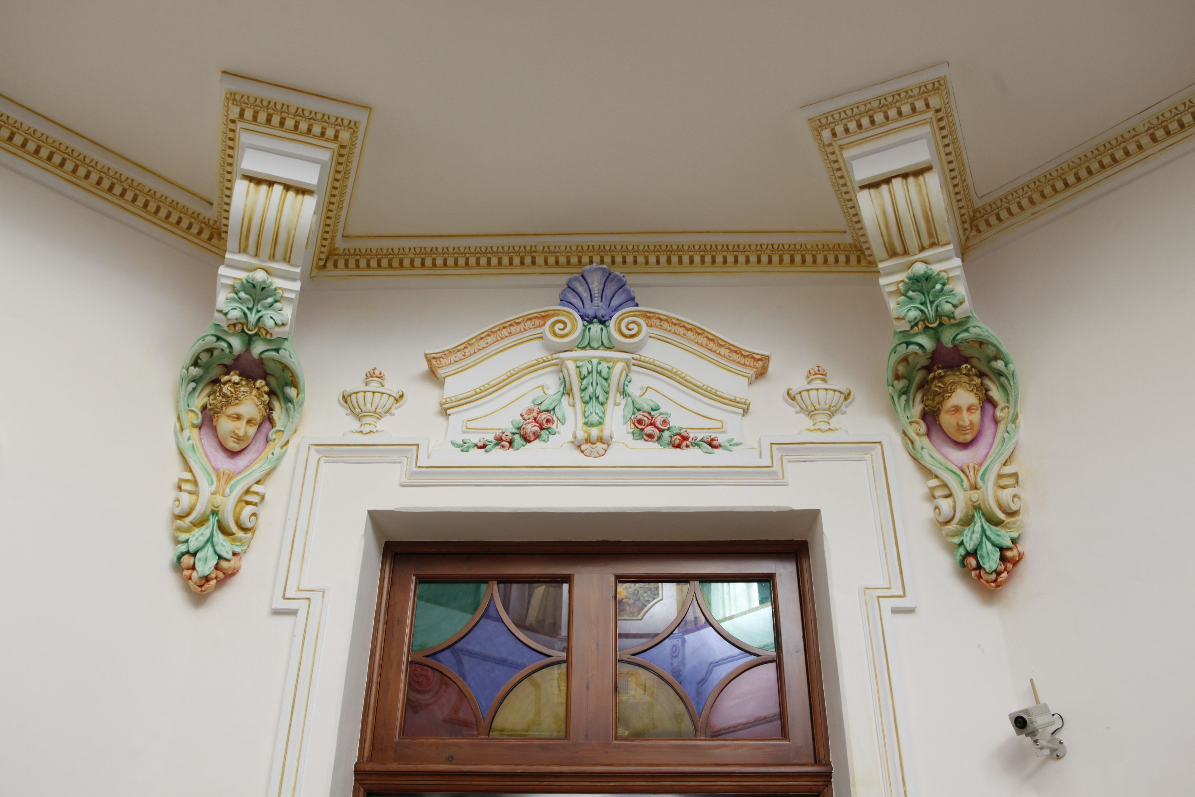 Una stanza con decorazioni elaborate alle pareti, una porta in legno e una telecamera di sicurezza.
