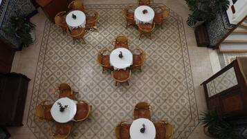 An overhead view of a hotel lobby with a patterned floor, multiple round tables with chairs, and potted plants.