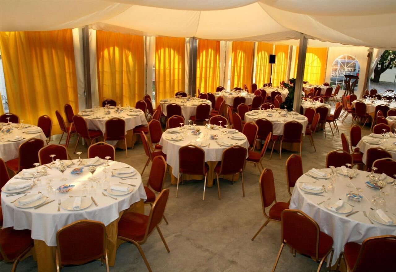 A banquet hall with round tables set for dining, red chairs, and yellow curtains.