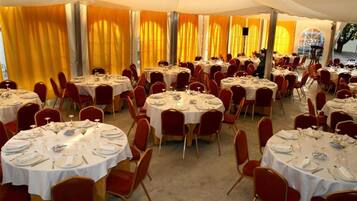 A banquet hall with round tables set for dining, red chairs, and yellow curtains.