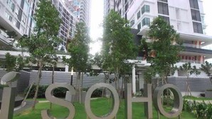 Un bâtiment moderne, reconnaissable à son grand panneau « SOHO », entouré de verdure et bordé d’une promenade piétonne.