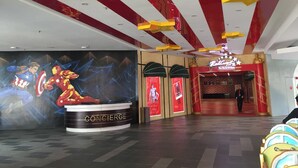 Un comptoir de réception orné d’une grande fresque représentant des super-héros, un plafond rayé de rouge et de blanc, et une entrée surmontée d’un tapis rouge.