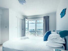 Una habitación de hotel con una cama grande, vistas de la ciudad a través de un ventanal y un balcón con barandilla.