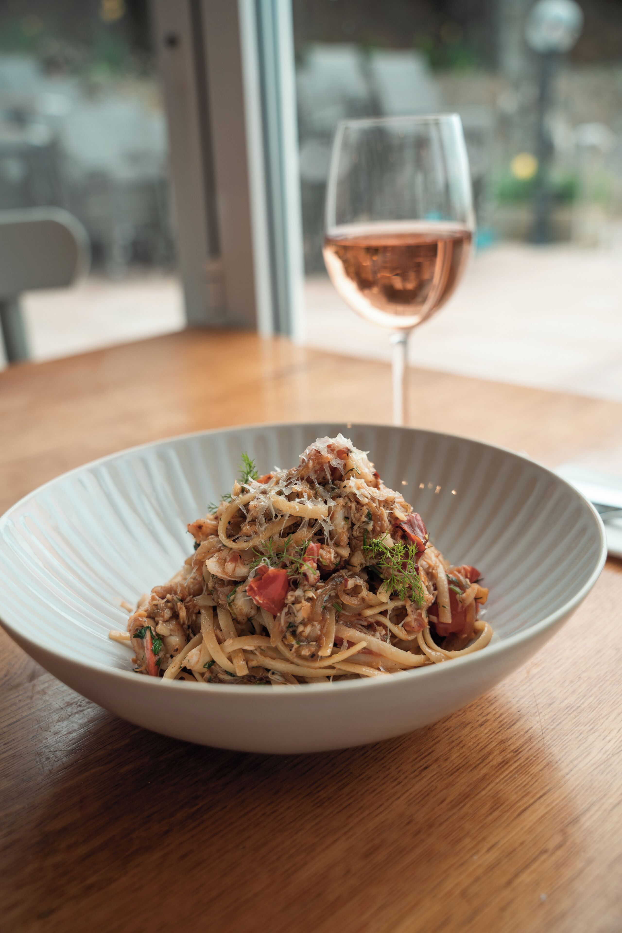 Un plat de pâtes accompagné d’un verre de vin, le tout posé sur une table en bois.