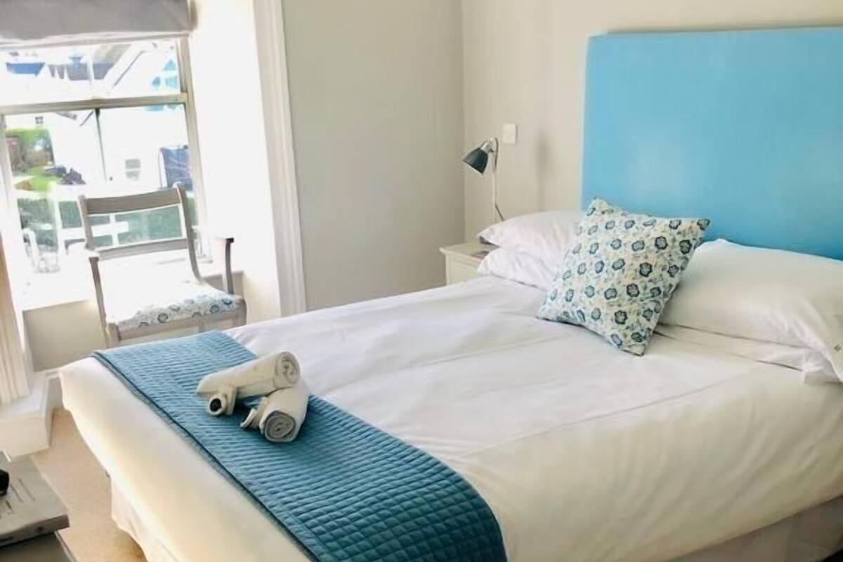 A neatly made bed with a blue blanket, a pillow with a pattern, and a pair of rolled-up towels on the bed.