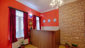 A room with a wooden reception desk, red curtains, a brick wall, and two potted plants. - Euphoria Inn (Tbilisi)