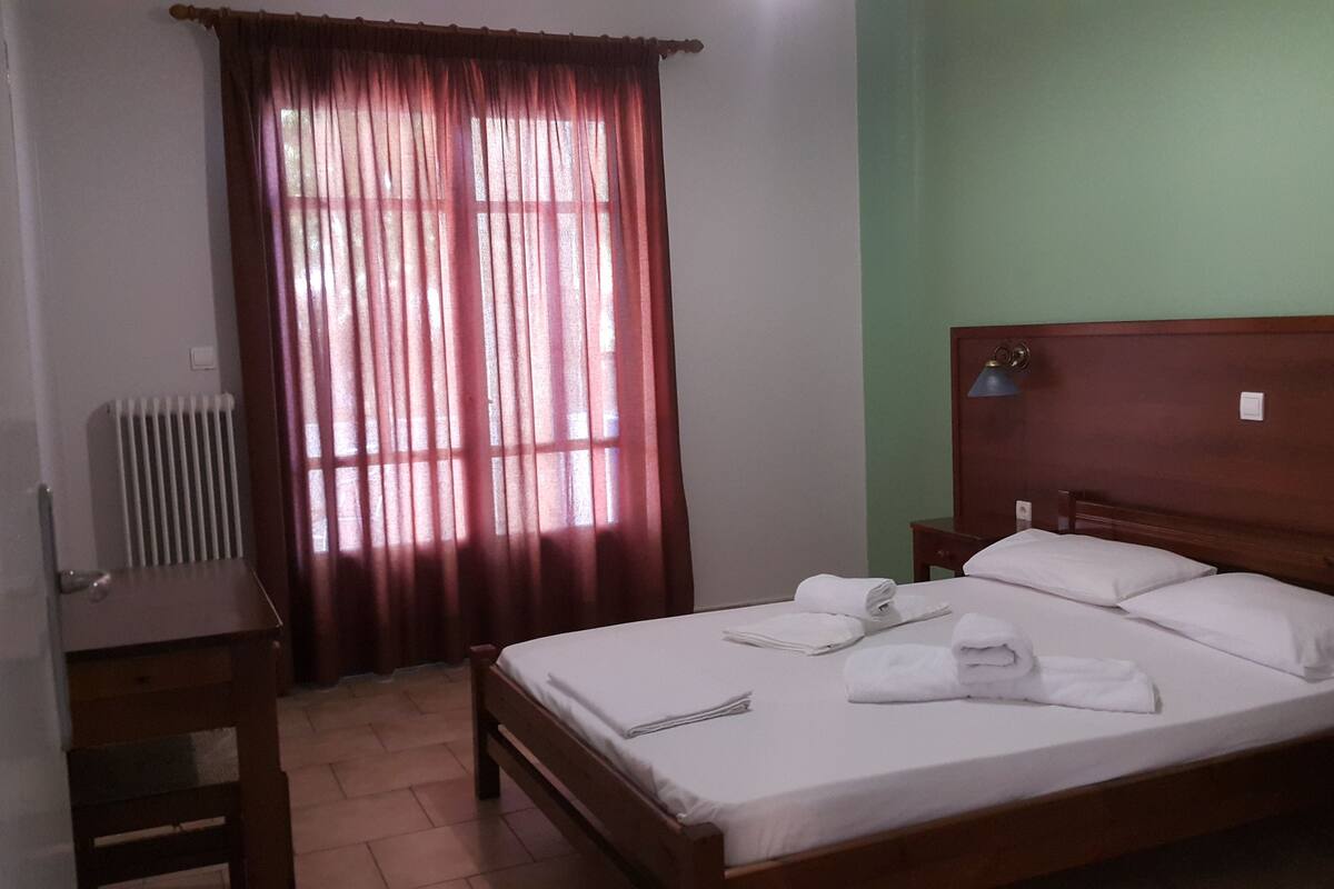 Un dormitorio con una cama de madera, un radiador, un escritorio y una ventana con cortinas.