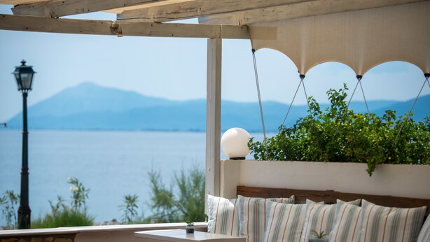 Un patio frente al mar con zona de estar acolchada, una mesita y vistas al mar y a las montañas.