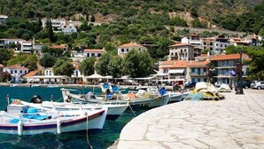 Un pueblo costero con barcos amarrados en un muelle, rodeado de casas escalonadas y abundante vegetación.