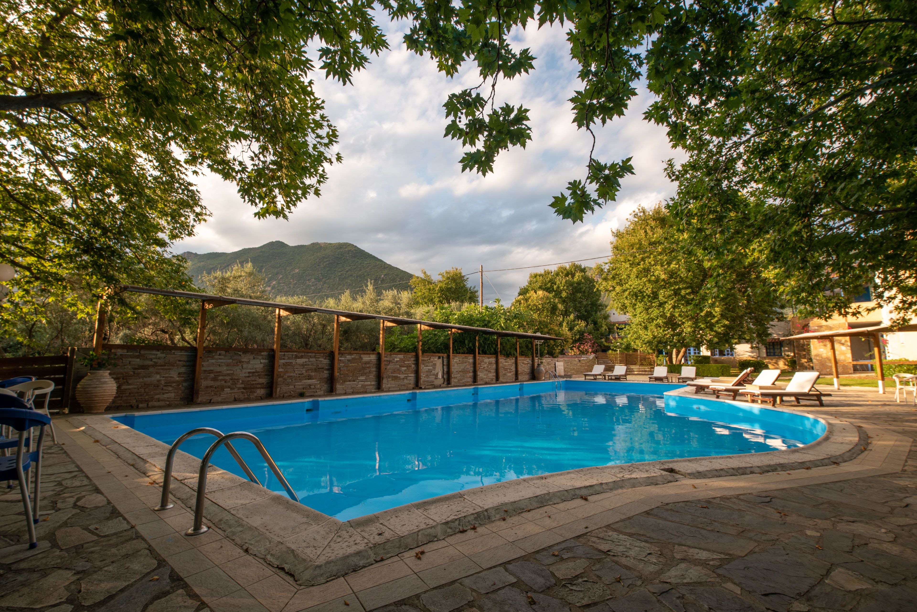 A swimming pool with a wooden deck, lounge chairs, and a view of mountains in the background.