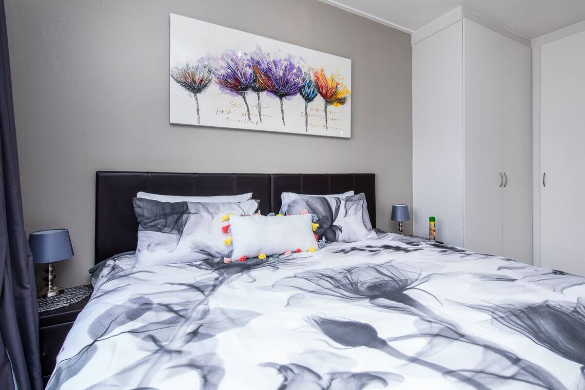 A bedroom with a bed, a nightstand, a lamp, a wardrobe, and a painting on the wall.