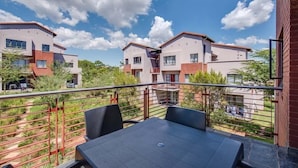 A balcony with a table and chairs, overlooking a residential area with modern buildings. - Jackal Creek Self-Catering Apartments (Roodepoort)