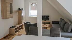 A modern living room with a built-in TV, a wooden entertainment unit, and a cozy seating area with a sofa and chairs. - FeWo Lerbachtal (Osterode am Harz)