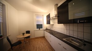 A compact kitchen with white cabinets, a black countertop, a sink, and a window with blinds. - FeWo Lerbachtal (Osterode am Harz)