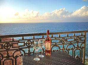 Una bottiglia di vino e due bicchieri su un tavolo con ringhiera metallica vista mare.