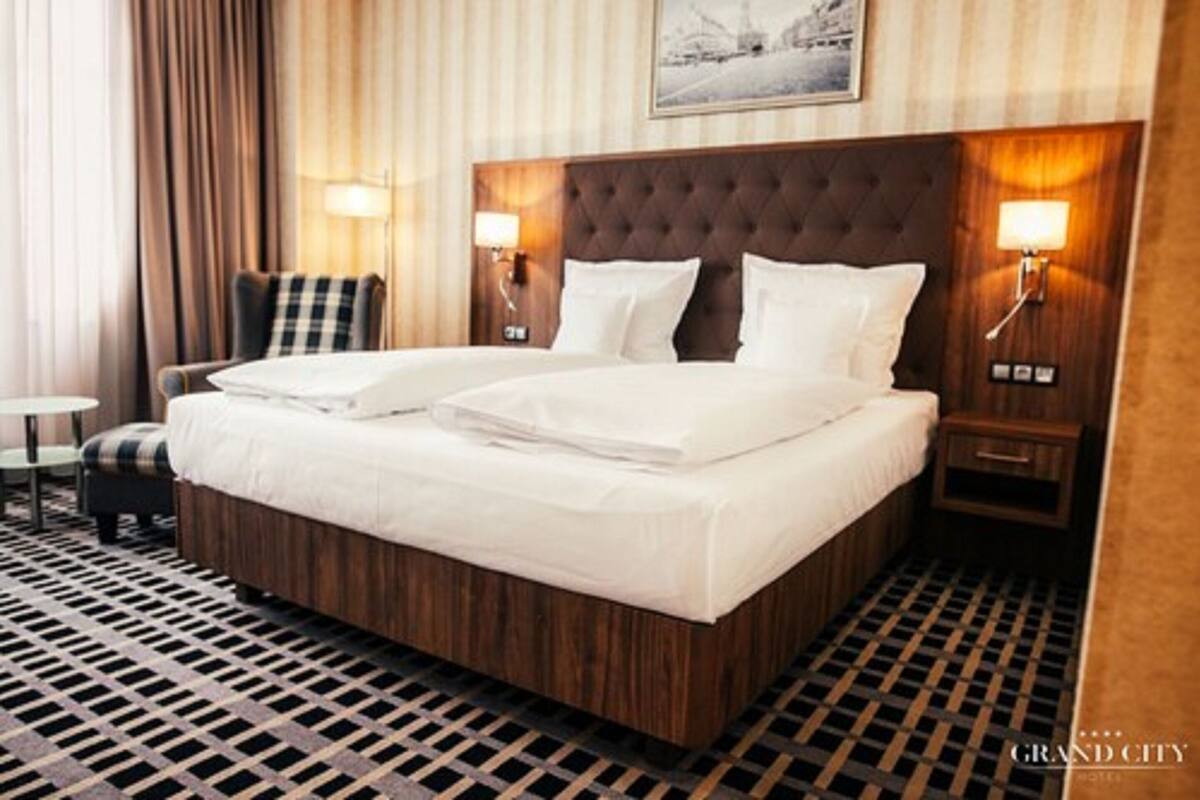 A hotel room with a large bed, two bedside tables with lamps, a chair, and a patterned floor.