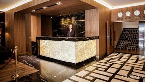 A hotel reception area with a marble counter, wooden paneling, and clocks displaying different cities. - Grand City Hotel Wrocław (Wroclaw)