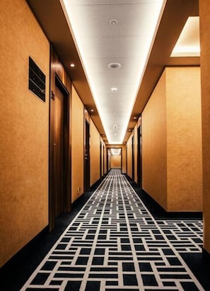 En hotellkorridor med ett mönstrat golv, trädörrar och infälld belysning.